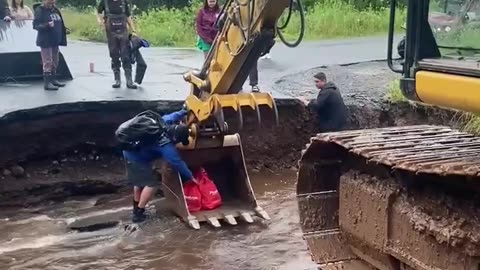 Man Uses Backhoe To Cross Washed Out Road and Bring Home Groceries