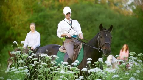 Young women ride on horseback through the field at sunset