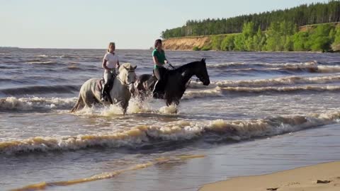 Two women ride on horse at river beach in water sunset light