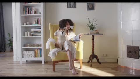 A Woman Having Coffee And Reading Magazine While Seated On A Chair With Her Dog