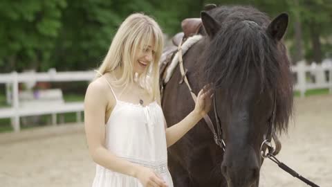 Milennial woman and horse at horse club stroking the horse and smiling at him