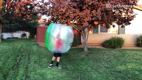 Teen kicks guy in bubble suit on grass