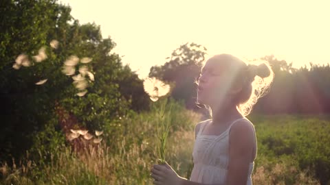 Girl playing with a dandelion flower in the sunset