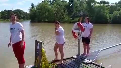 Three girls swan dive into lake off small wooden platform pier
