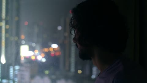 Man Looking Out of City Window at Night