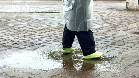 the feet of a child splashing in a puddle in a raincoat