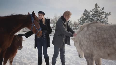 Portrait young couple stroking horses on a country ranch in the winter season