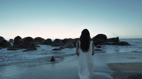 Woman walking on beach towards boulders