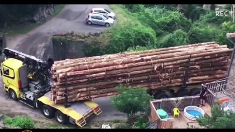 An extra-long trailer loaded with lumber passes through a small bridge.