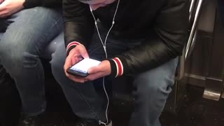Guy on subway on phone headphones aren't plugged in