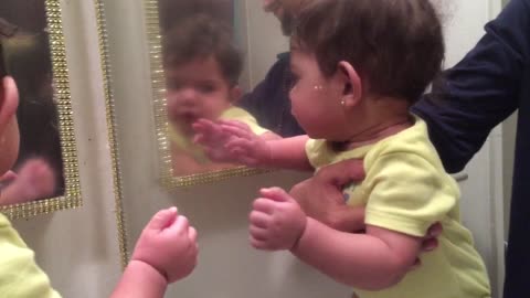 Baby girl attempts to make contact with her mirror reflection