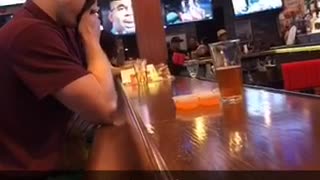 Guy in red shirt sitting at bar holds back his vomit with a napkin