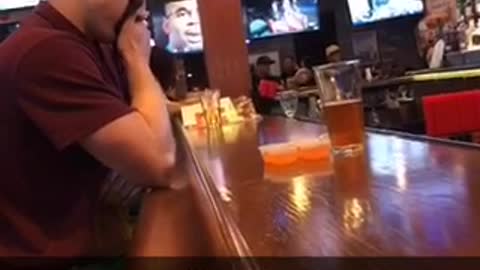 Guy in red shirt sitting at bar holds back his vomit with a napkin
