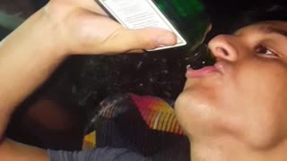 Guy in blue shirt chugs alcohol in green bottle