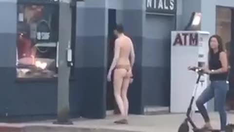Guy in tiger print speedo shirtless standing in front of store