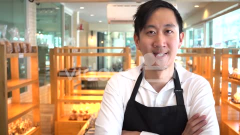 Asian cafe restaurant shop owner having arms crossed with assortments of cakes behind