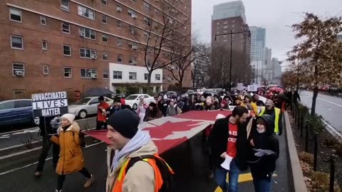 Hundreds of NYC workers carry an American and Canadian flag while they shut down the Brooklyn bridge to fight the mandates