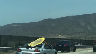 Yellow surf board on grey silver car roof