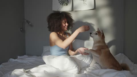 A Woman Teasing Her Pet Dog With Food While In Bed