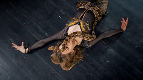 Attractive woman in bright costume dance lying on the floor with a snake