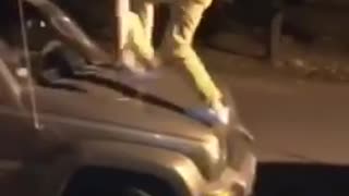 Guy jumps onto jeep and then falls onto black car and falls onto ground