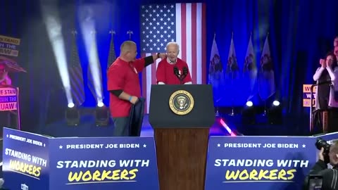 Biden requires some assistance as he struggles to put on a t-shirt he was given before his speech