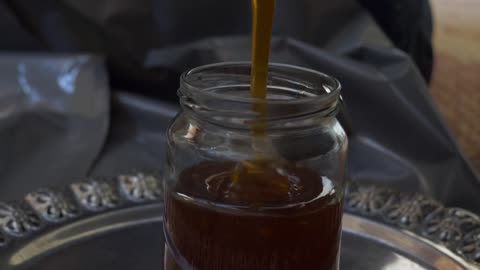 A beekeeper filling jars with honey after the honey extraction process