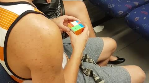 Guy in white orange shirt rubix cube on train