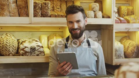 Young Man Bread Seller Scrolling And Taping On The Tablet Computer While Standing At The Counter In