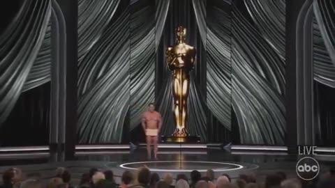 Watch as John Cena shocks the crowd by presenting an award completely naked, only covered by a sign