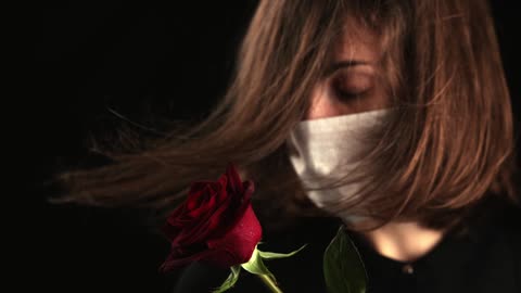 Girl with face mask looking at the red Rose