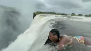 Woman laying down inches before a massive 380 feet drop, devils pool - Victoria falls