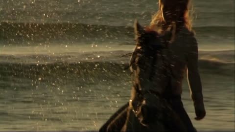 Woman on horse at seashore, riding through surf