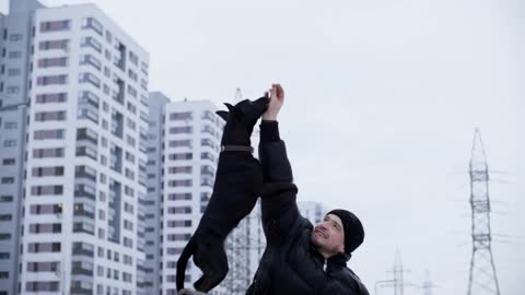 Man handler training black dog to stand on its hind legs on winter walk