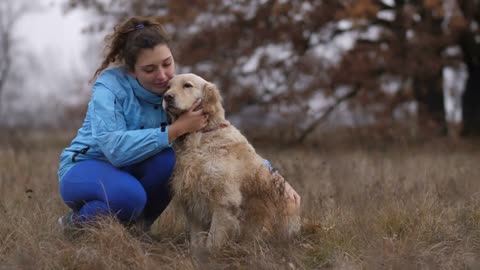 Positive cheerful young woman caressing gently her labrador retreiver in autumn nature