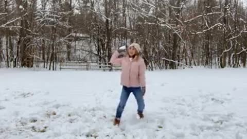 Husband makes his wife engage in playing throwing snow with him when she talking on the stream.