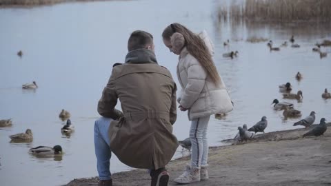 Wide shot portrait of pretty brunette girl talking with young father on riverbank