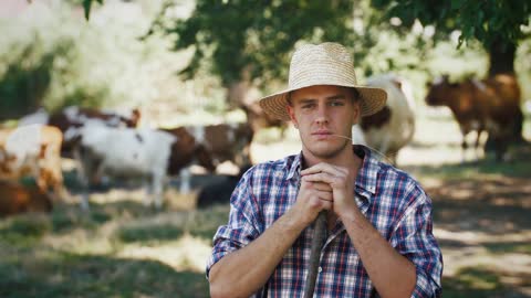 Portrait of young villager man shepherd in straw hat with his flock of cows on a rural background