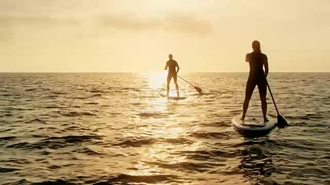 Woman standup paddling behind the man at sunset stock video...