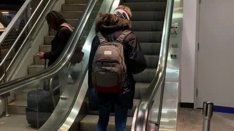 Man black jacket back pack wrong side of escalator