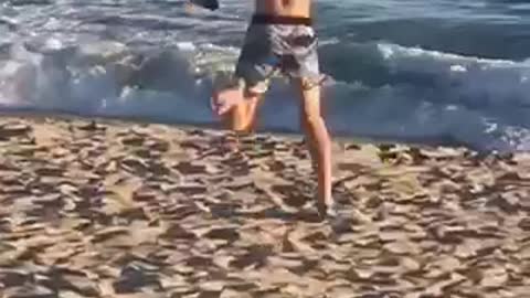 Guy blue shorts running funny on beach toward water