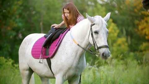 Young woman climbs on a white horse in summer meadow