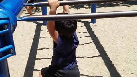 Little kid black shirt monkey bars face plants into sand woodchips