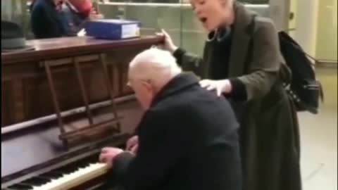 The old man is playing the piano, and the passing girls are singing along with it.