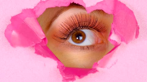 Eye of a woman peeking out of the hole of a pink paper screen
