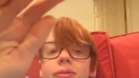Ginger kid with glasses sitting on red couch dabbing