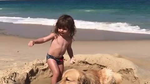 Golden Retriever becomes part of little girl's sandcastle