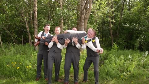 Four guys pick up groom to take picture and hold him sideways on three they throw him up and he drops onto ground