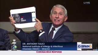 Fauci holding up a paper that says "Fire Dr. Fauci"