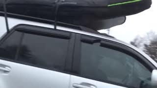 Silver car drives with surfboard on top of car